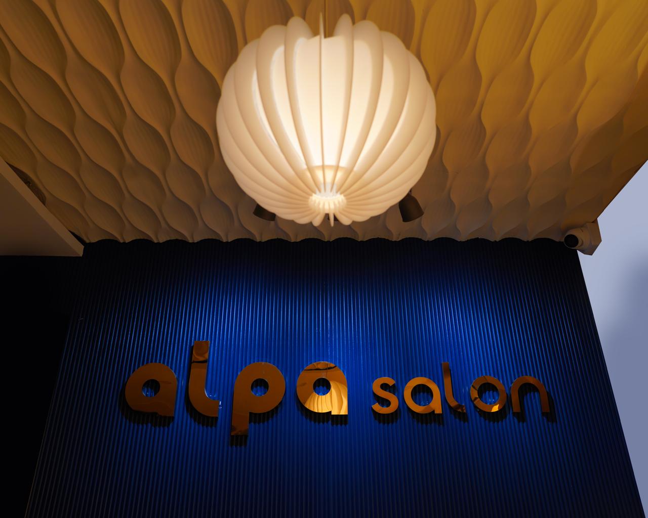 Gold 'alpa salon' letters on the ribbed cobalt wall under the sculptural pendant lamp